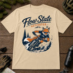 Sand tee featuring a sunglasses-wearing fox carving a mountain bike berm, with the phrase “Flow State Activated.”