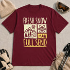 Maroon tee featuring a retro ski and mountain graphic with the phrase “Fresh Snow, Full Send.”