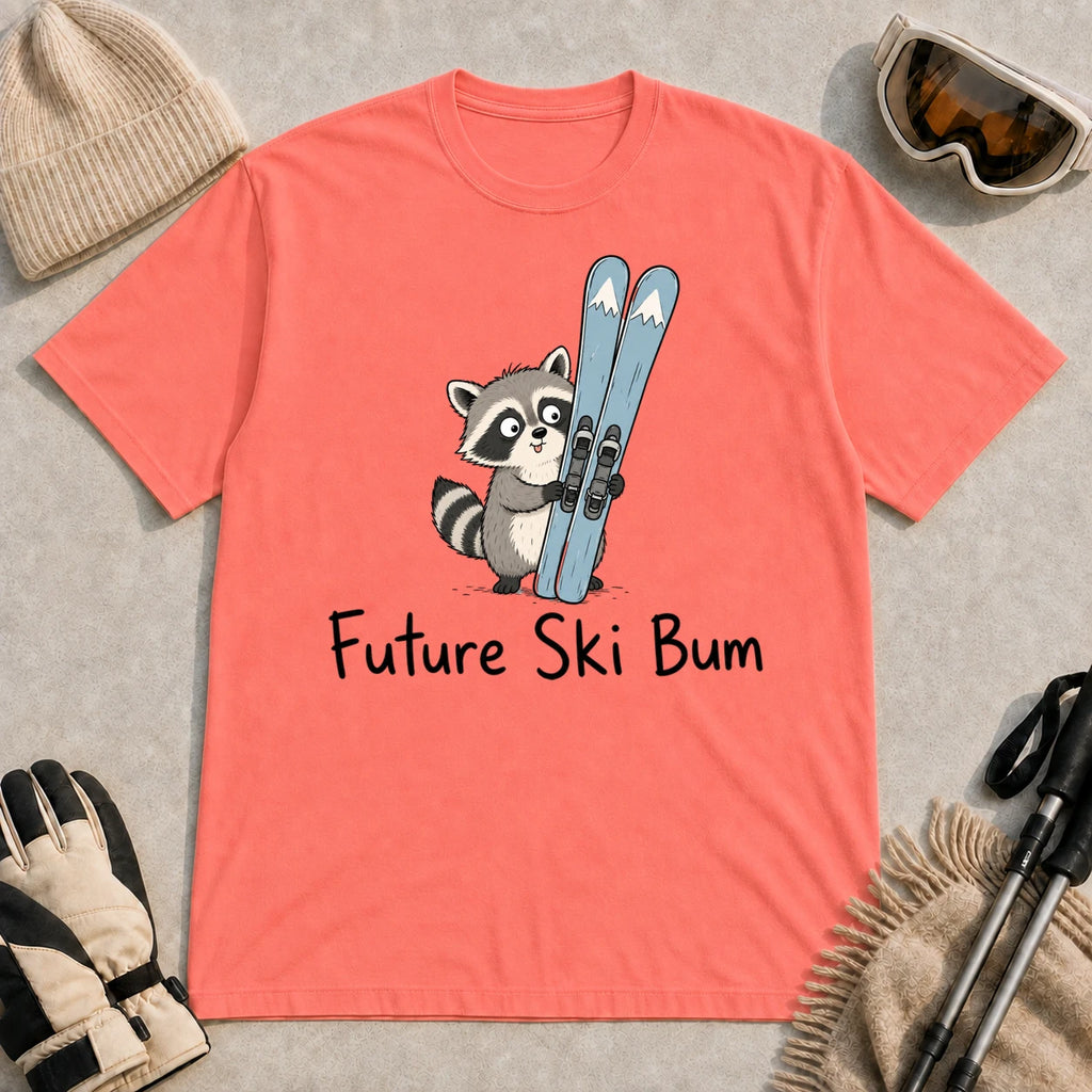 Coral Silk tee featuring a cute raccoon standing beside a pair of skis, with the phrase “Future Ski Bum.”
