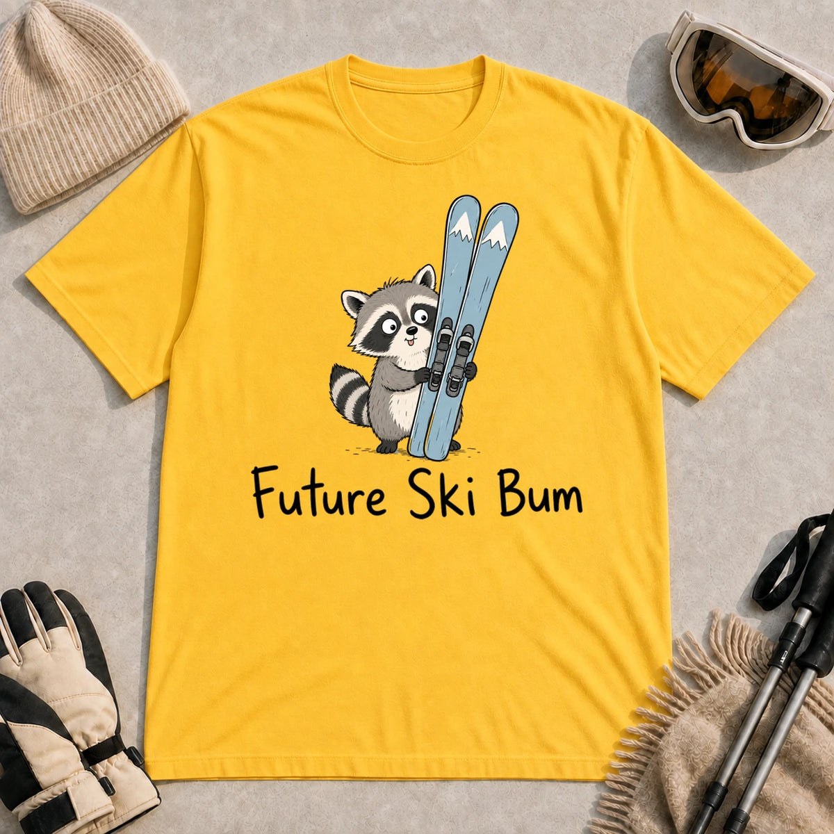 Daisy tee featuring a cute raccoon standing beside a pair of skis, with the phrase “Future Ski Bum.”