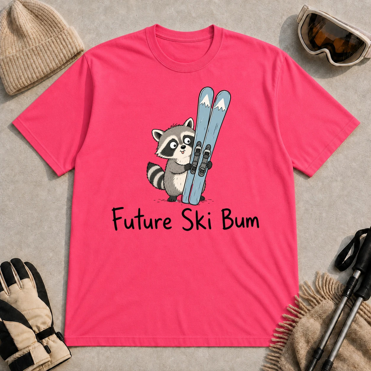 Heliconia tee featuring a cute raccoon standing beside a pair of skis, with the phrase “Future Ski Bum.”