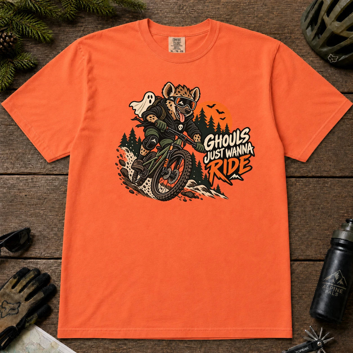 Burnt Orange tee featuring a hyena mountain biking through a spooky Halloween trail scene with a ghost, bats, and orange moon beside the phrase “Ghouls Just Wanna Ride.”
