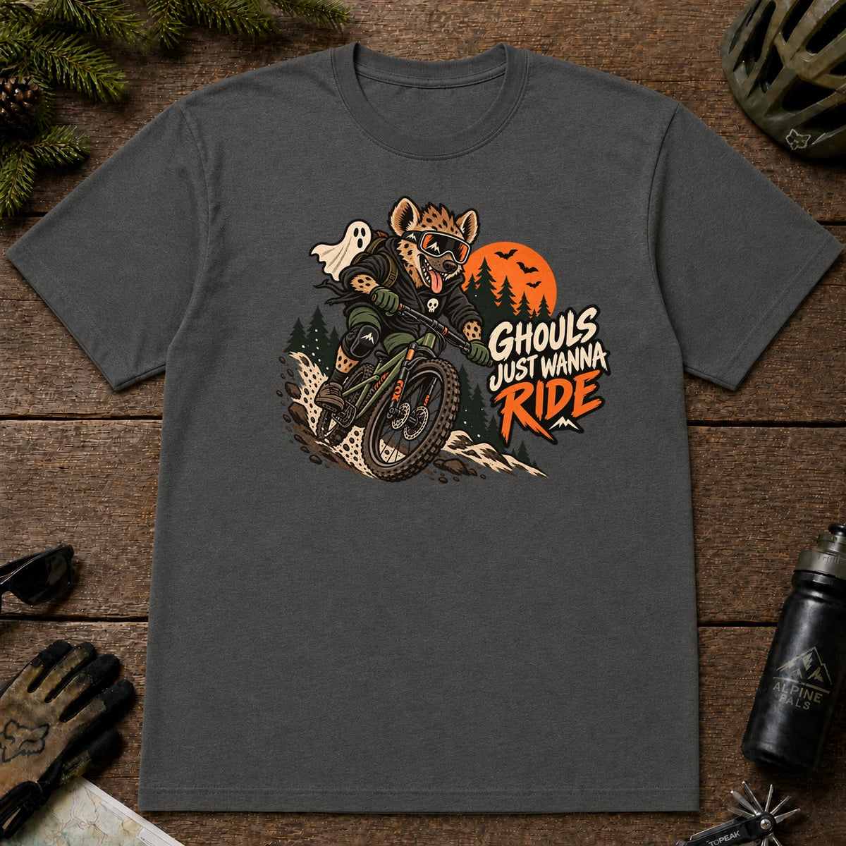 Dark Heather Gray tee featuring a hyena mountain biking through a spooky Halloween trail scene with a ghost, bats, and orange moon beside the phrase “Ghouls Just Wanna Ride.”