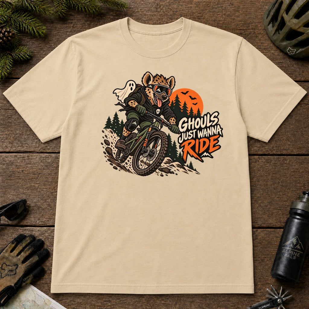 Sand tee featuring a hyena mountain biking through a spooky Halloween trail scene with a ghost, bats, and orange moon beside the phrase “Ghouls Just Wanna Ride.”