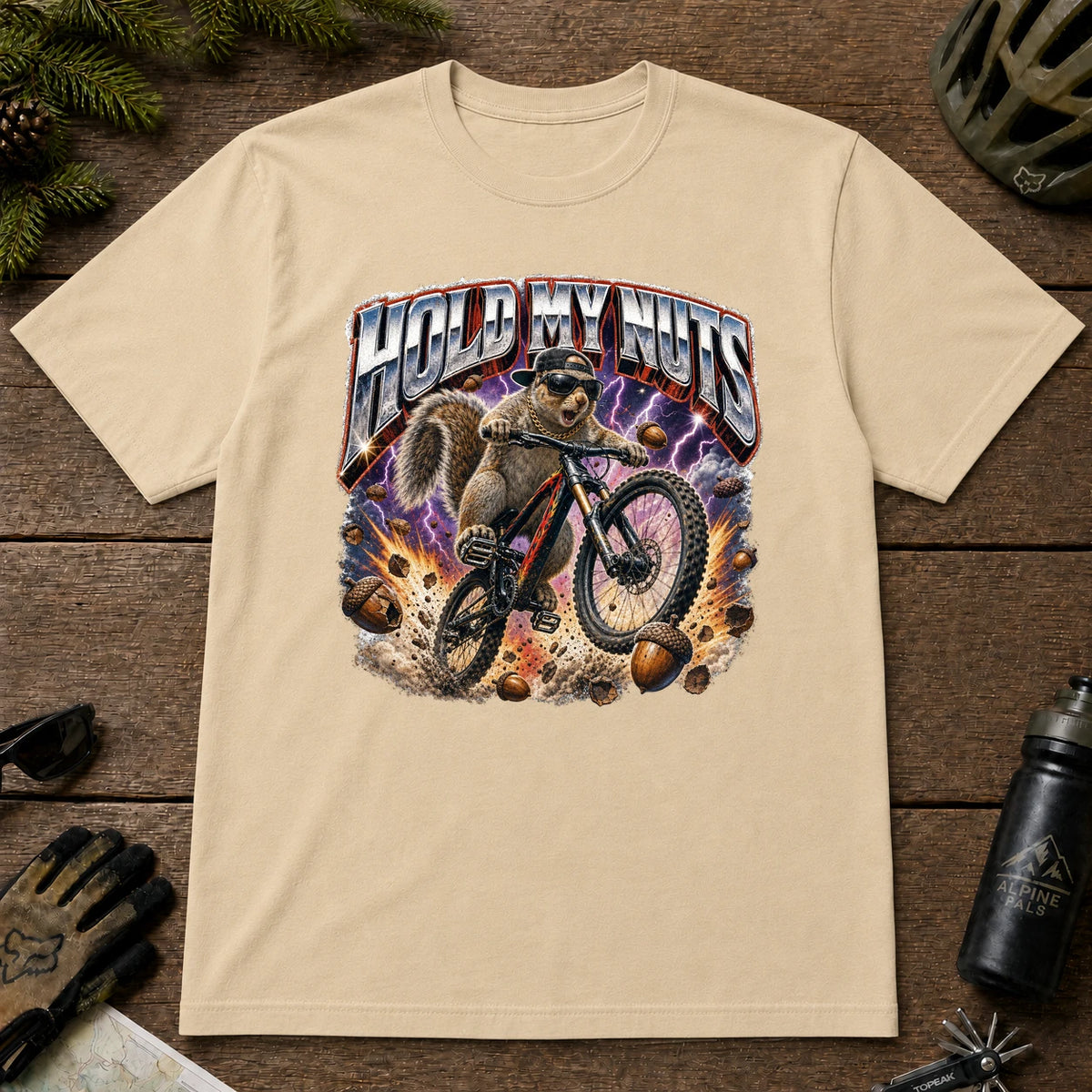 Sand t-shirt featuring a wild squirrel mountain biking through flying acorns and lightning beneath the bold phrase “HOLD MY NUTS.”