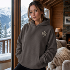 Woman wearing a charcoal gray hoodie with a logo in a cozy room with a snowy mountain view.