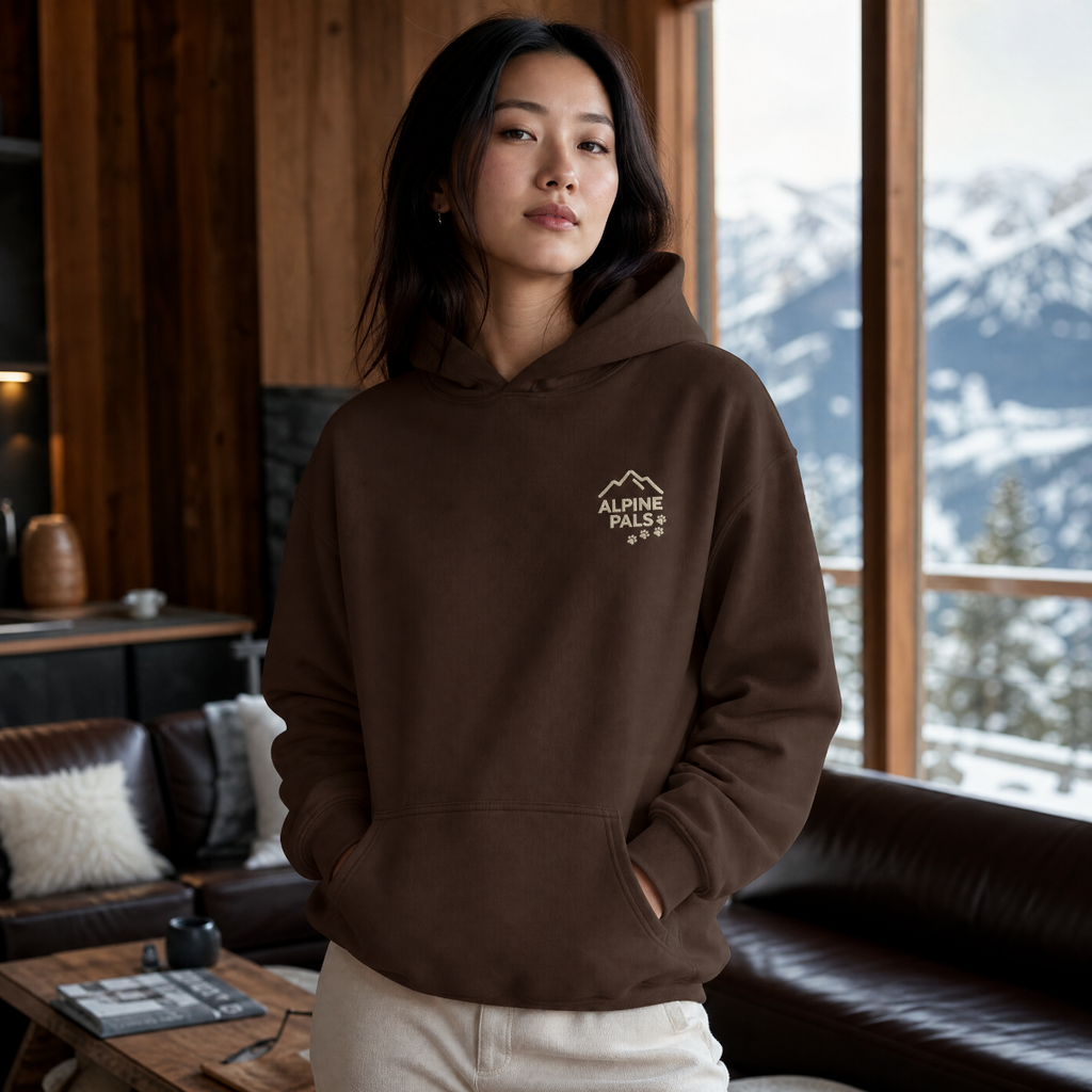 Woman wearing a dark chocolate brown hoodie with a logo, standing in a room with a snowy mountain view.