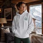 Woman wearing a ash gray hoodie with a logo, standing in a cozy room with mountain view.