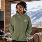 Woman wearing a military green hoodie with 'Alpine Pals' logo in a cozy living room with mountain view.