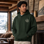 Man wearing a forest green hoodie with 'Alpine Pals' logo in a cozy living room with mountain view.