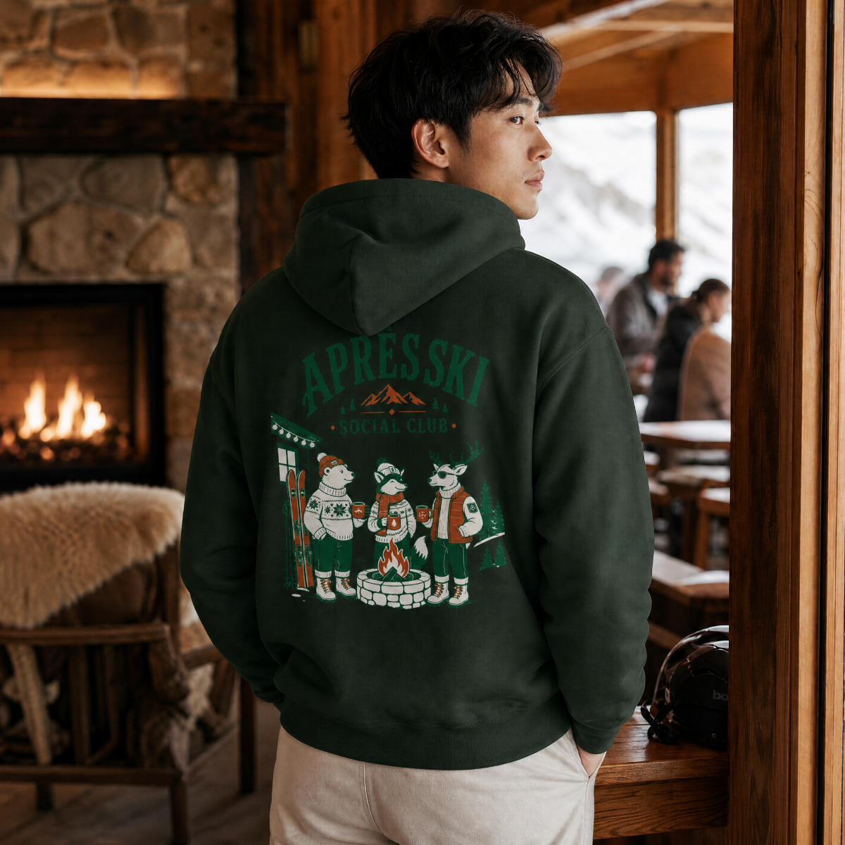 Person wearing a forest green hoodie with a graphic design in a cozy indoor setting.