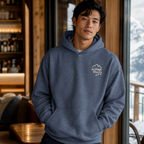 Man wearing a heather sport dark navy hoodie with 'Alpine Pals' logo indoors.