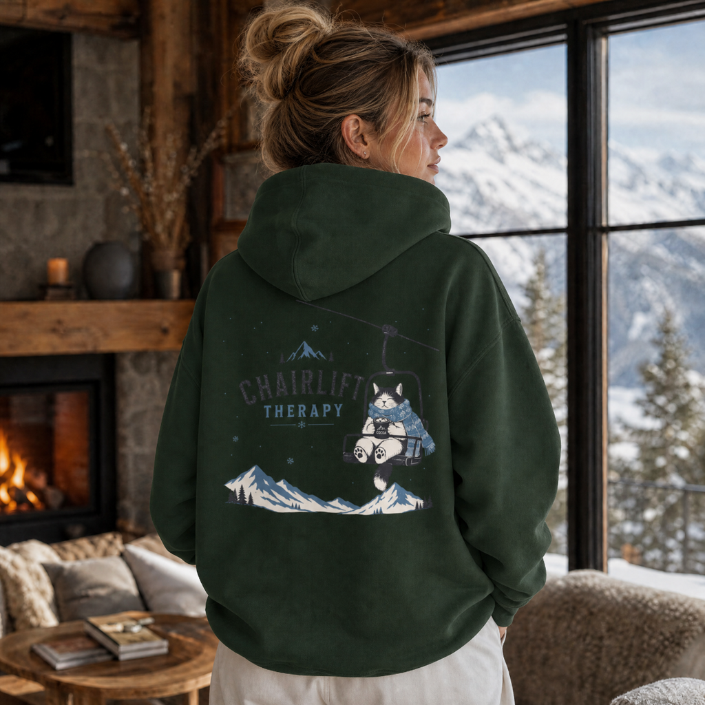 Person wearing a hoodie with a mountain design and text, standing in a cozy room with a view of mountains.