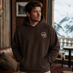Man wearing a dark chocolate brown hoodie with 'Alpine Pals' logo indoors.