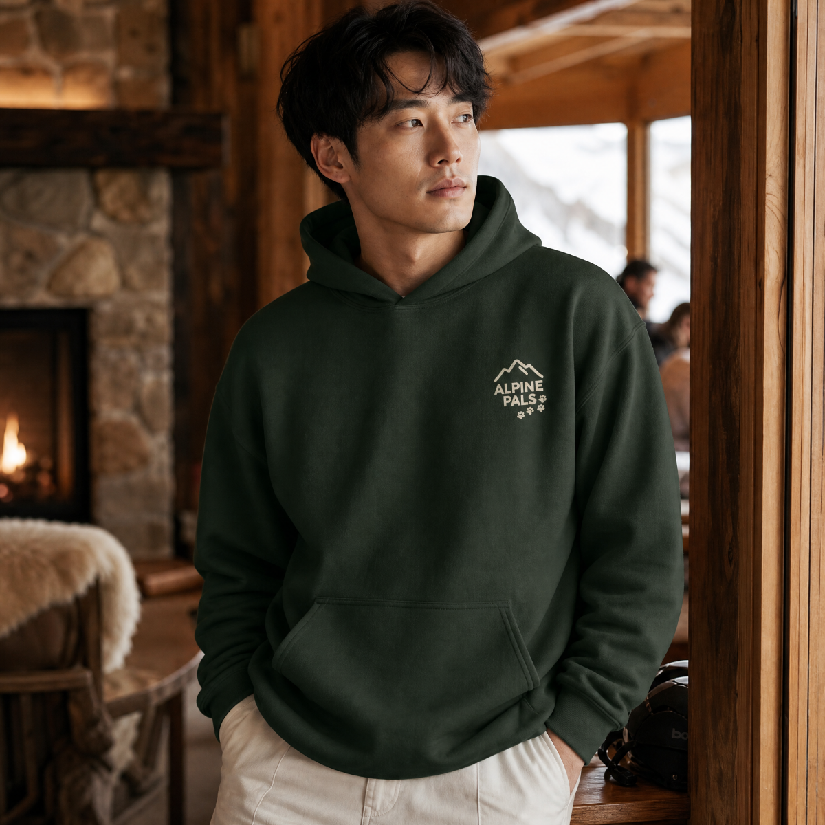 Man wearing a forest green hoodie with a logo in a cozy indoor setting