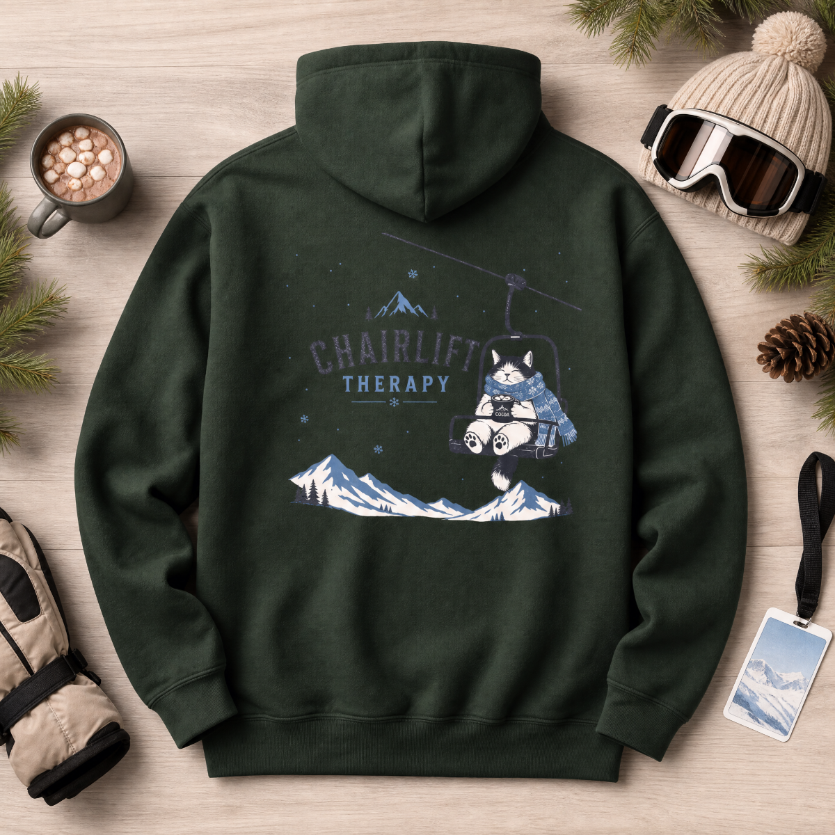Forest green hoodie with 'Chairlift Therapy' graphic on a wooden surface with winter accessories.