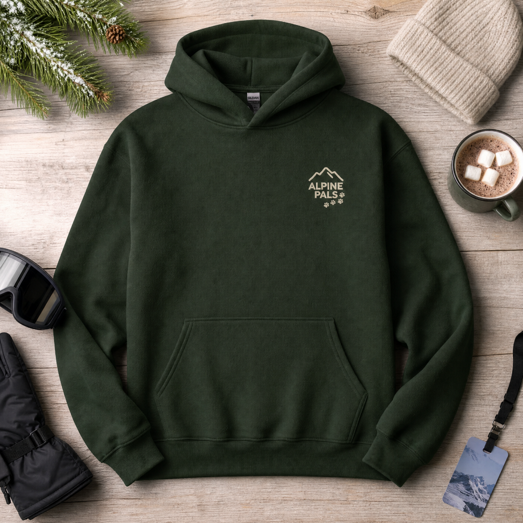 Forest green hoodie with 'Alpine Pals' logo on a wooden surface with winter accessories.