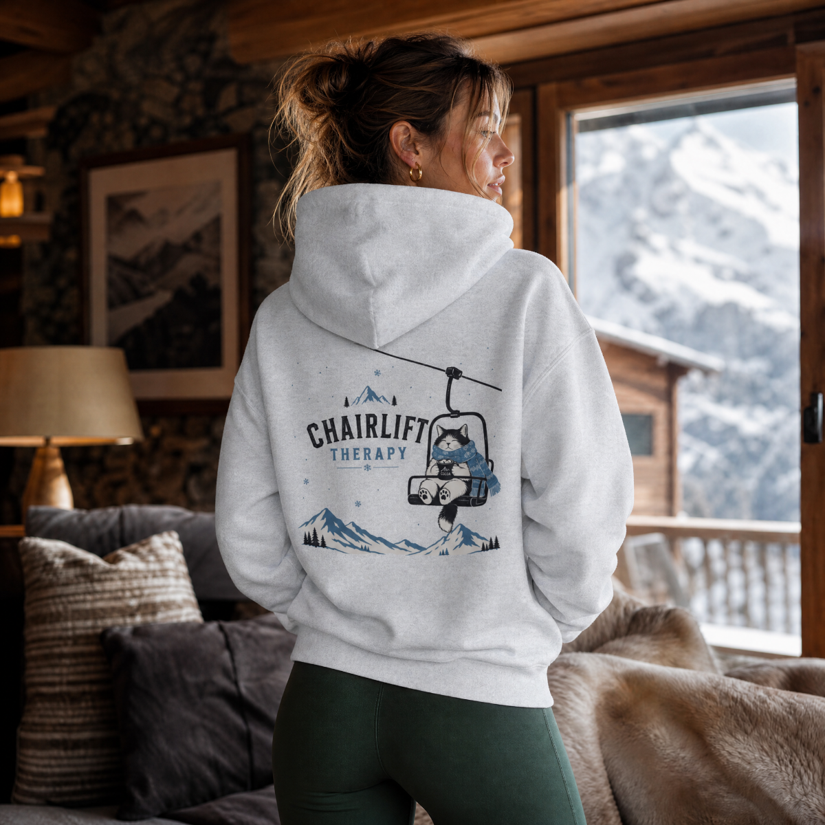 Person wearing a hoodie with a chairlift graphic in a cozy living room with mountain view.