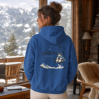 Person wearing an indigo blue hoodie with a chairlift graphic, standing in a cozy room with a snowy mountain view.
