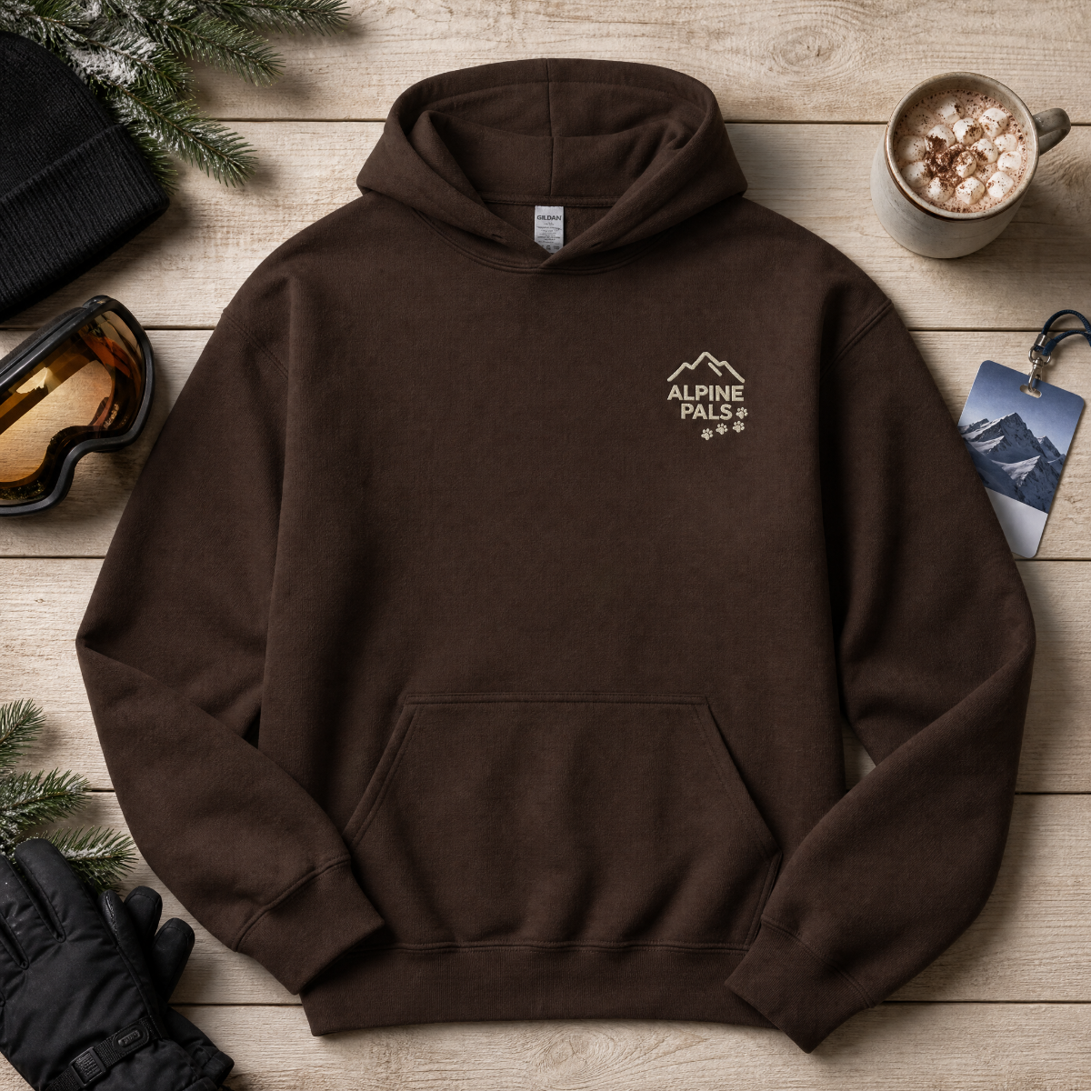 Dark chocolate brown hoodie with 'Alpine Pal' logo on a wooden surface with winter accessories.