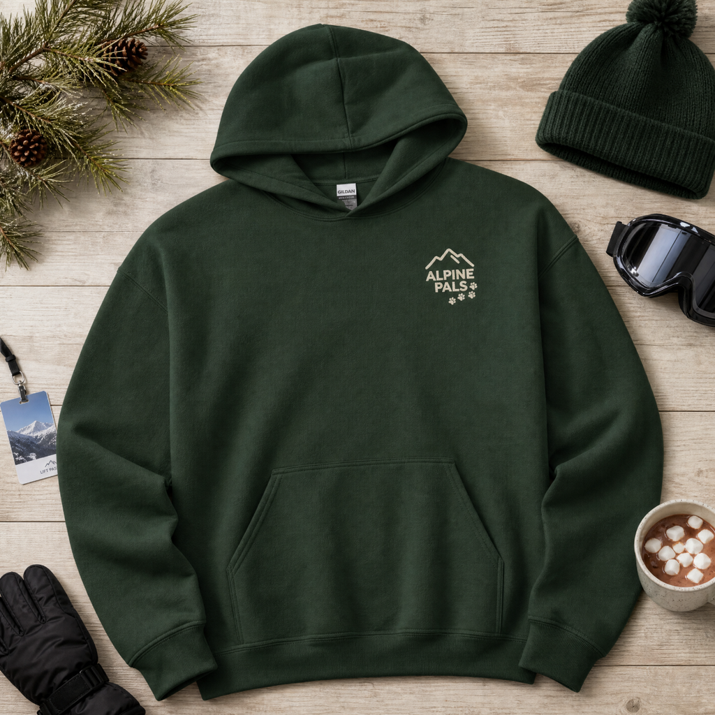 Forest green hoodie with 'Alpine Pals' logo on a wooden surface with winter accessories.