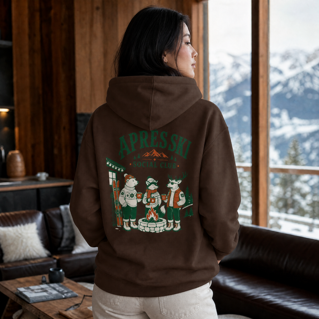 Person wearing a dark chocolate brown hoodie with 'Apres Ski Social Club' design, standing in a room with a snowy mountain view.