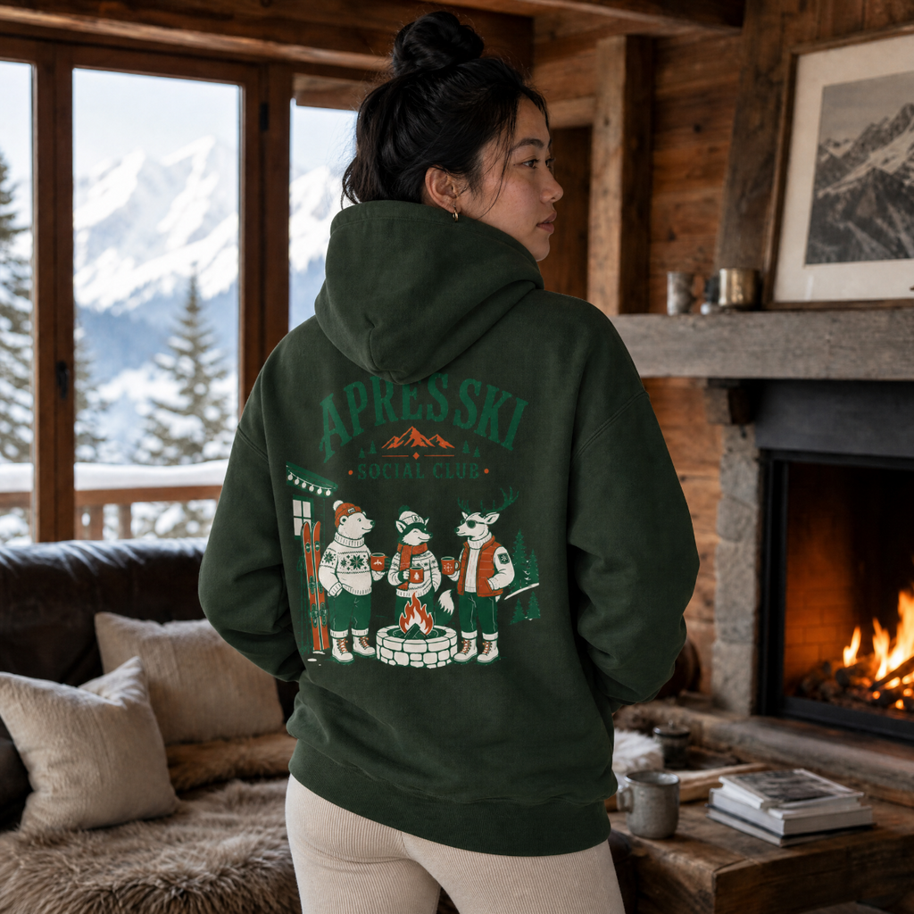 Person wearing a forest green hoodie with a graphic design in a cozy living room with a fireplace and mountain view.