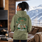 Person wearing a military green hoodie with 'Apres Ski Social Club' design, standing in a cozy room with mountain view.