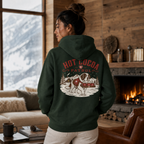 Person wearing a hoodie with 'Hot Cocoa Patrol' design in a cozy living room with a fireplace and mountain view.
