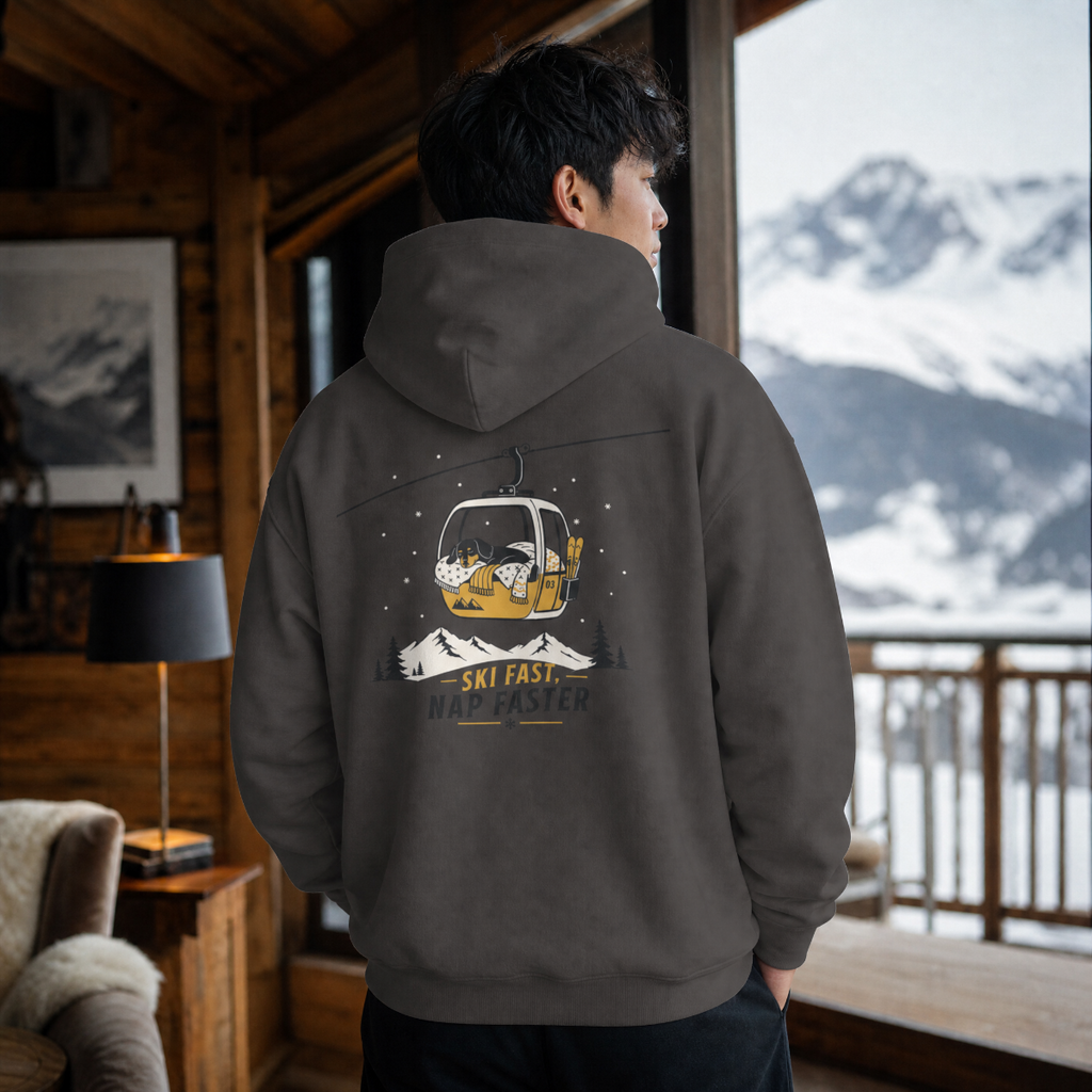 Person wearing a hoodie with a mountain graphic in a cozy room with a view of snow-covered mountains.