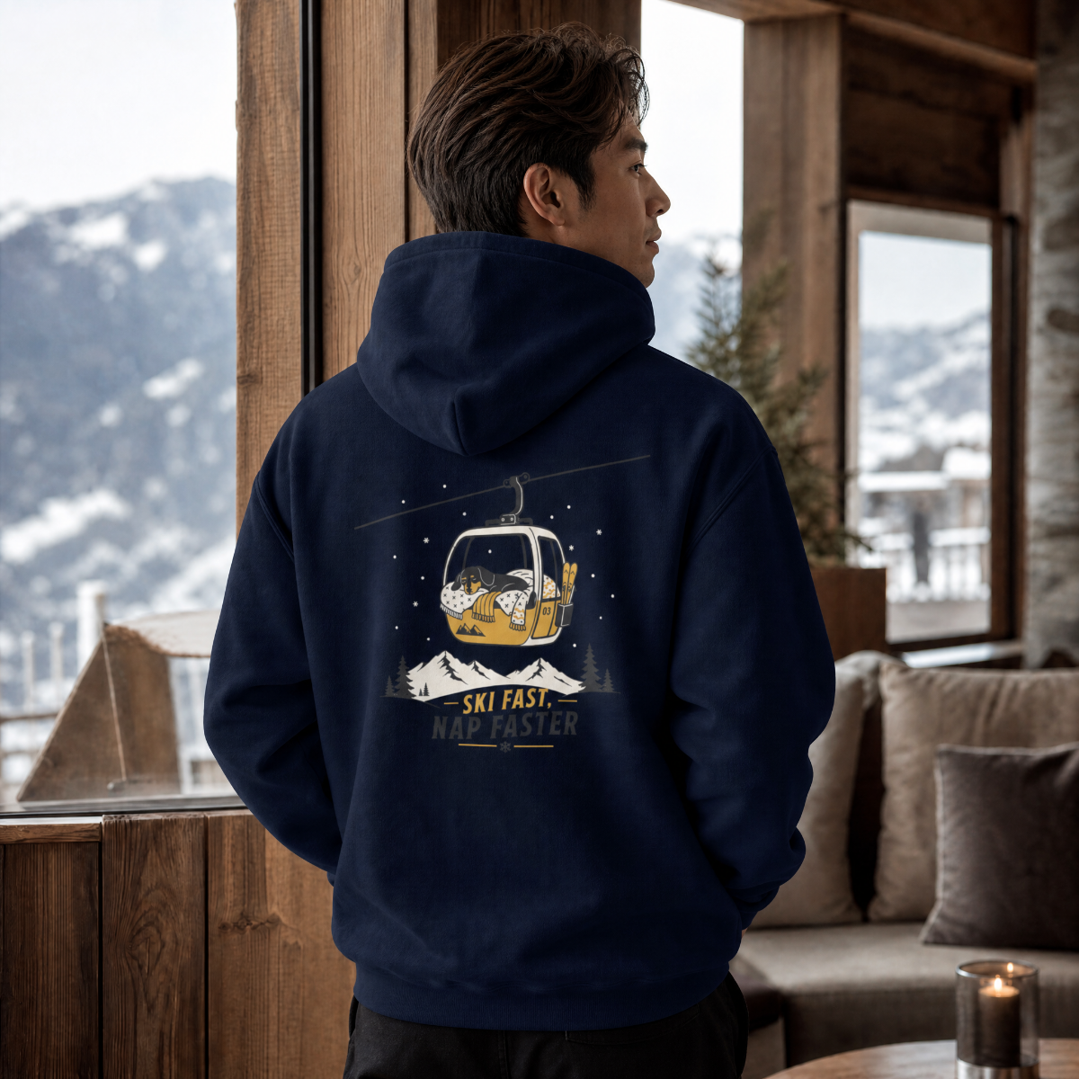 Person wearing a navy hoodie with a ski-themed design, standing in a cozy room with mountain views.