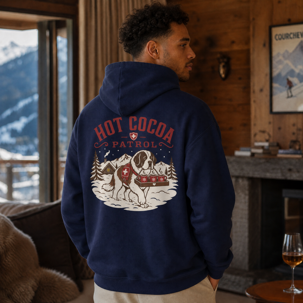 Man wearing a hoodie with a 'Hot Cocoa Patrol' design in a mountain cabin setting.