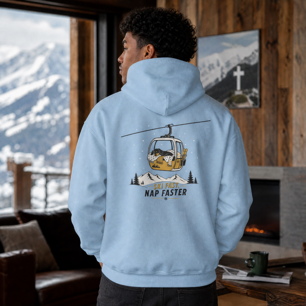 Person wearing a light blue hoodie with a mountain graphic and text, standing in a cozy room with a snowy mountain view.