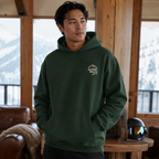 Man wearing a forest green hoodie with 'Alpine Pals' logo indoors