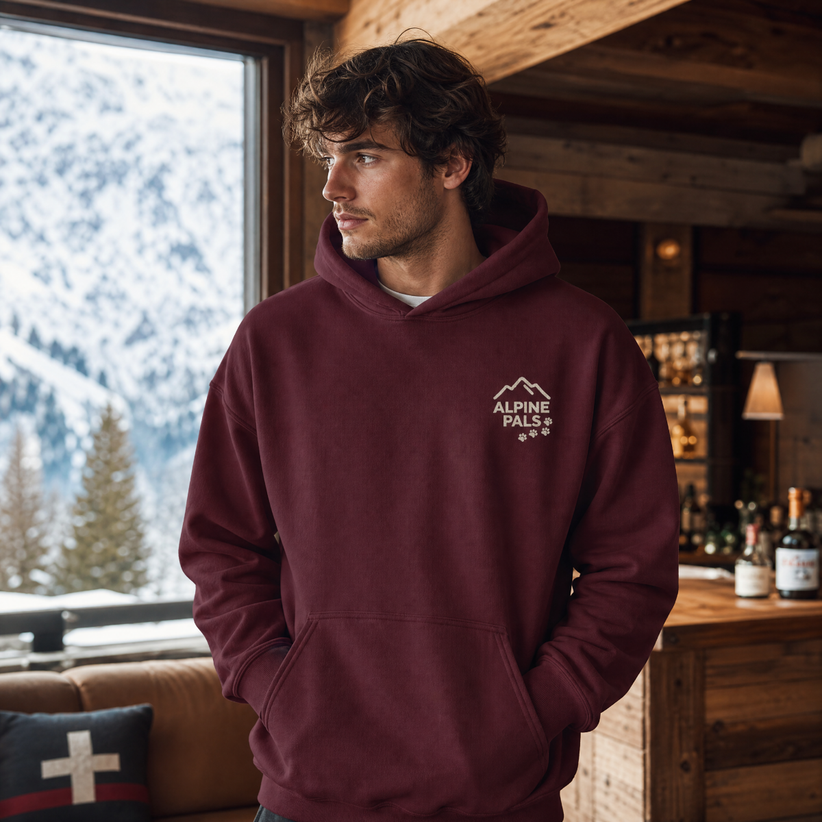 Man wearing a maroon hoodie with 'Alpine Pals' logo in a cozy room with mountain view