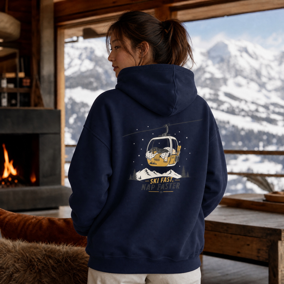Person wearing a navy hoodie with a mountain and ski lift design, standing in front of a window with a snowy mountain view.