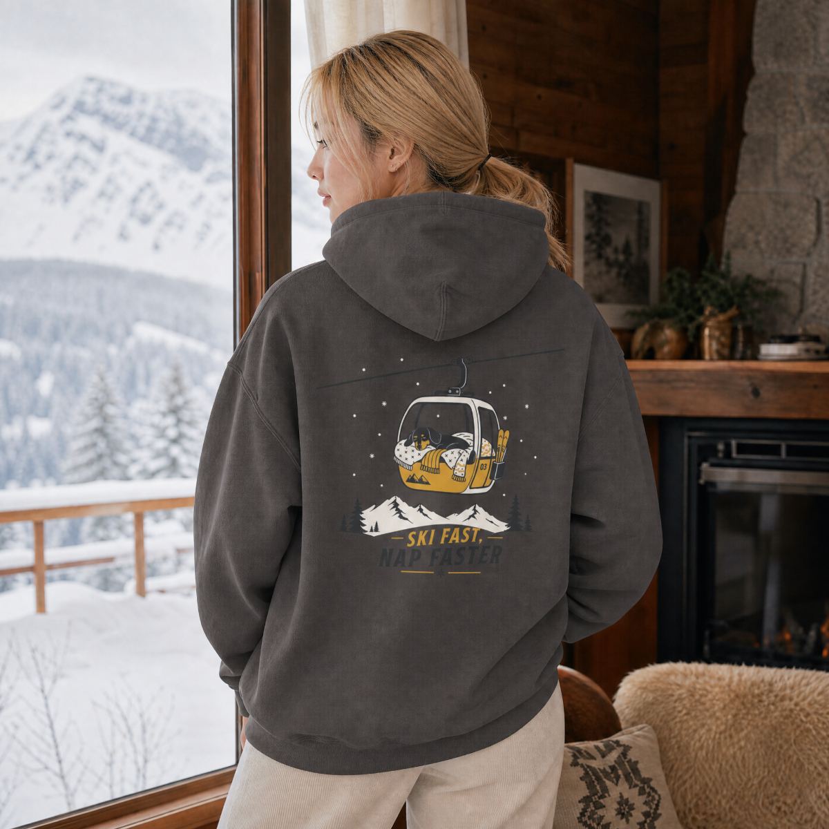 Person wearing a hoodie with a ski-themed design, looking out at snowy mountains.
