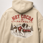 Sand colored hoodie with 'Hot Cocoa Patrol' graphic featuring a dog and hot cocoa on a tray.