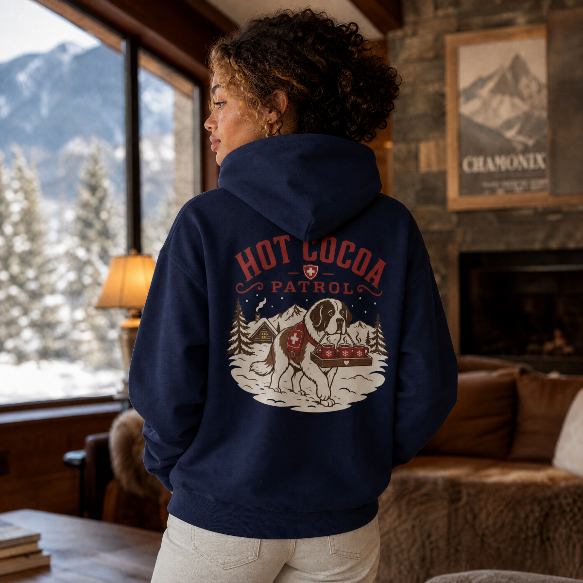 Person wearing a navy hoodie with 'Hot Cocoa Patrol' design in a cozy room with a mountain view.