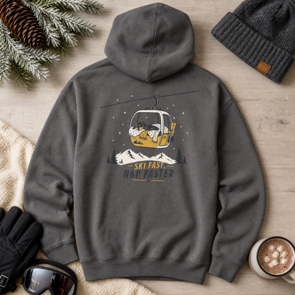 Charcoal gray hoodie with a ski lift graphic and text, surrounded by winter accessories on a wooden surface.