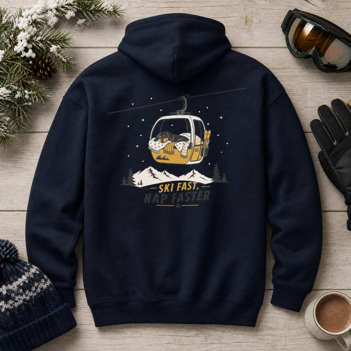 Navy blue hoodie with a ski-themed graphic on a wooden surface with winter accessories.