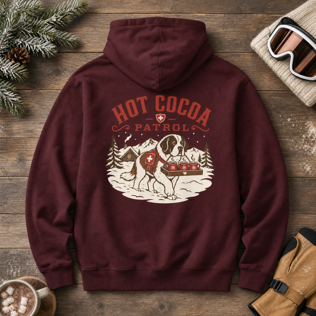 Maroon hoodie with 'Hot Cocoa Patrol' graphic on a wooden surface with winter accessories.