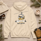 Sand colored hoodie with a graphic design on the back, placed on a wooden surface with winter accessories.
