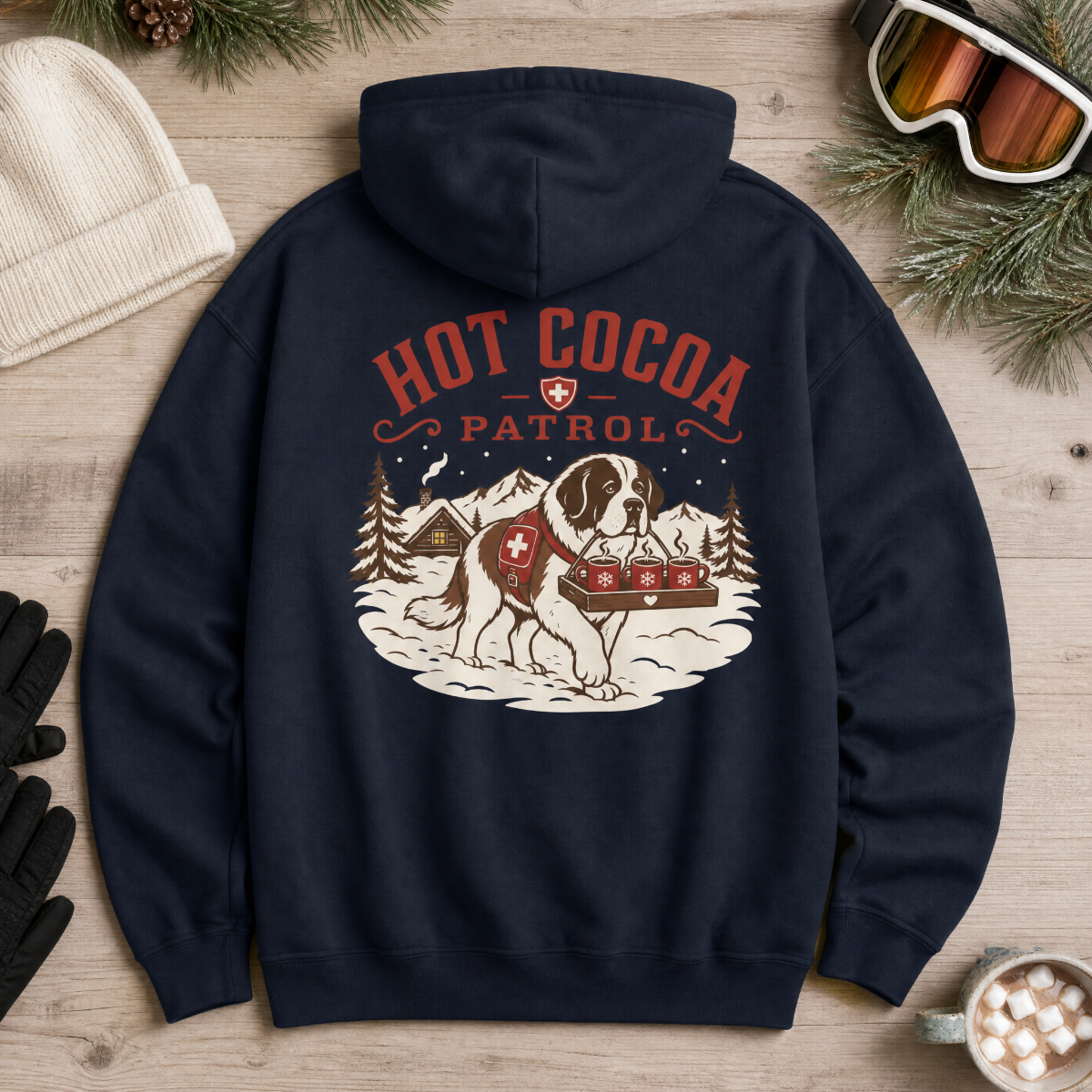 Navy blue hoodie with 'Hot Cocoa Patrol' graphic on a wooden surface with winter accessories.