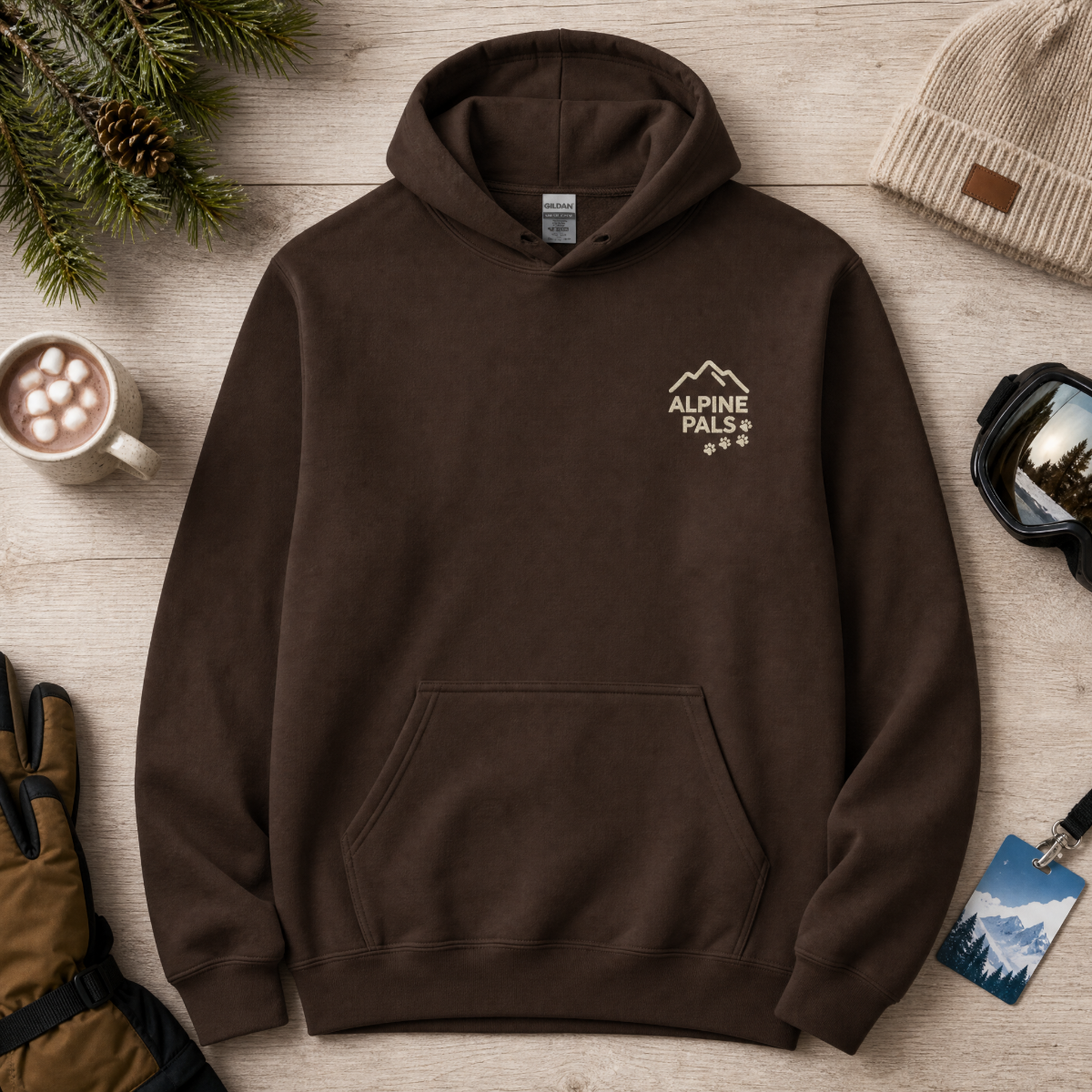 Dark chocolate brown hoodie with 'Alpine Pals' logo on a wooden surface with winter accessories.