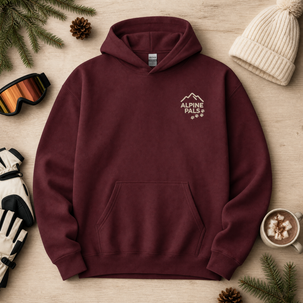 Maroon hoodie with 'Alpine Pals' logo on a wooden surface with winter accessories.