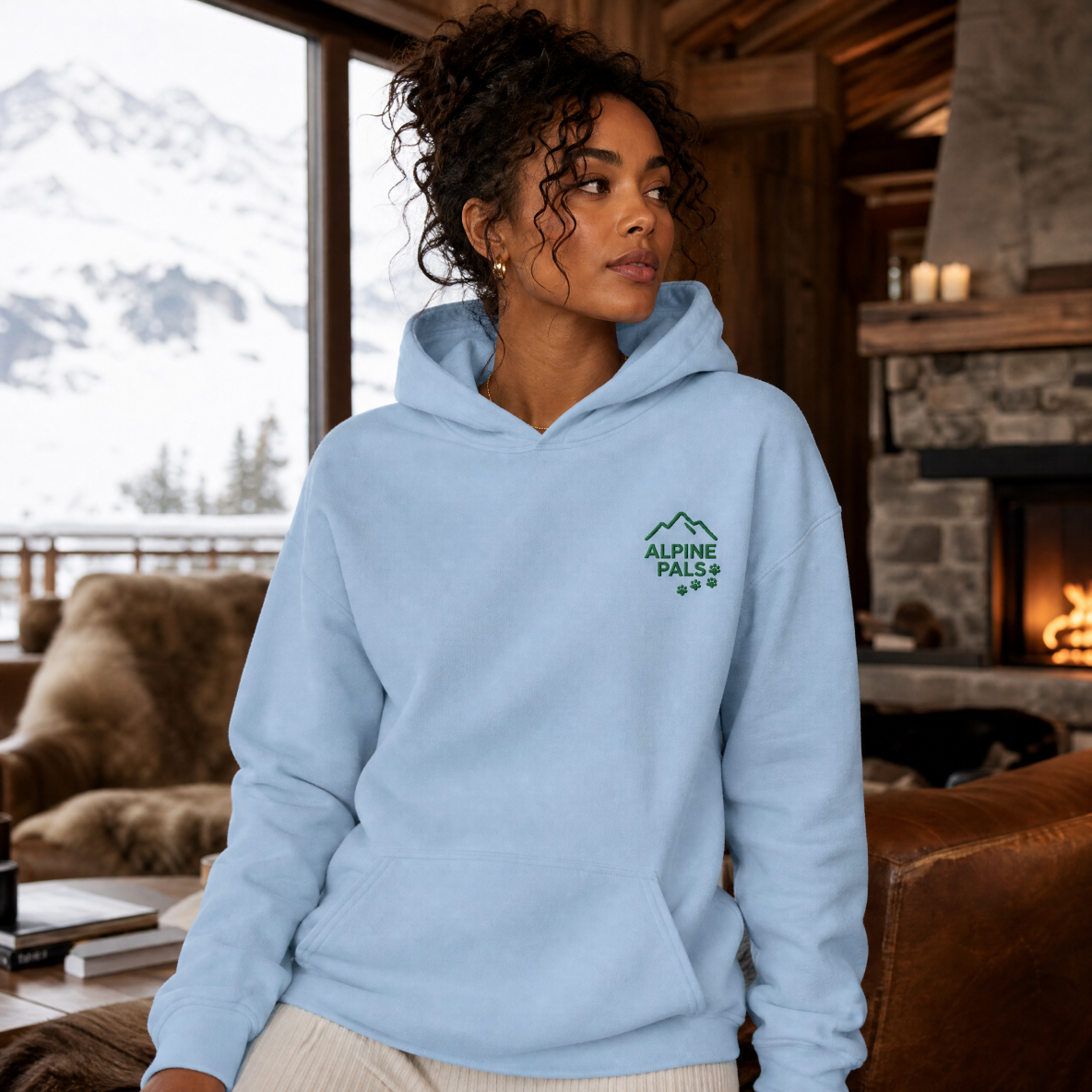 Woman wearing a light blue hoodie with an 'Alpine Peak' logo in a cozy living room.