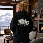 Woman wearing a black hoodie with a mountain graphic in a cozy living room with a view of mountains.