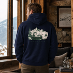 Man wearing a navy hoodie with a mountain graphic, standing in a cozy room with a window view of mountains.
