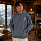 Man wearing a heather sport dark navy hoodie with a mountain logo in a cozy cabin setting.